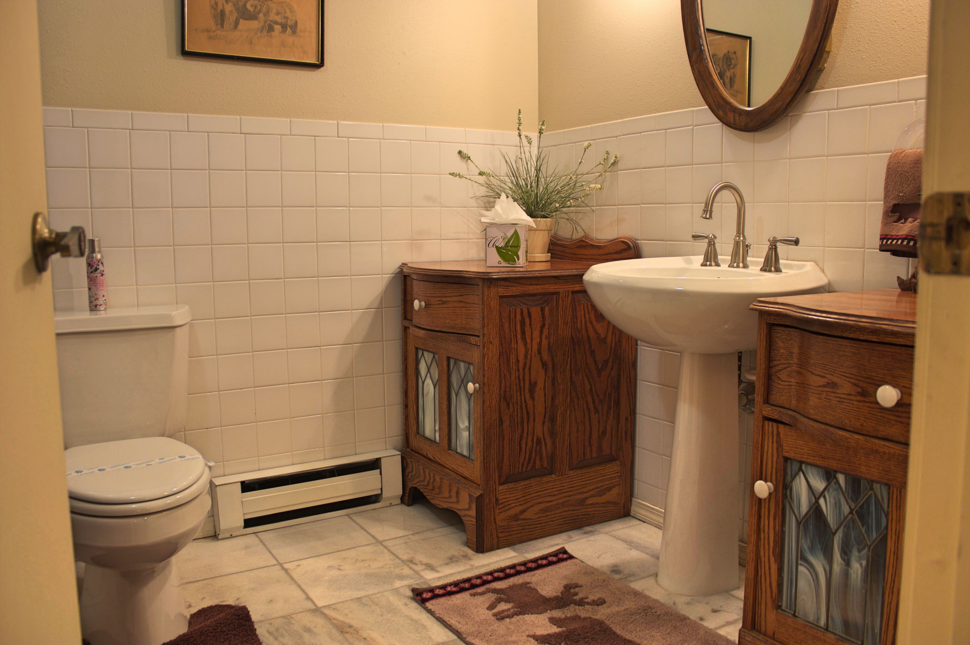 A bathroom with a toilet, sink, wooden cabinets, a mirror, and a potted plant.