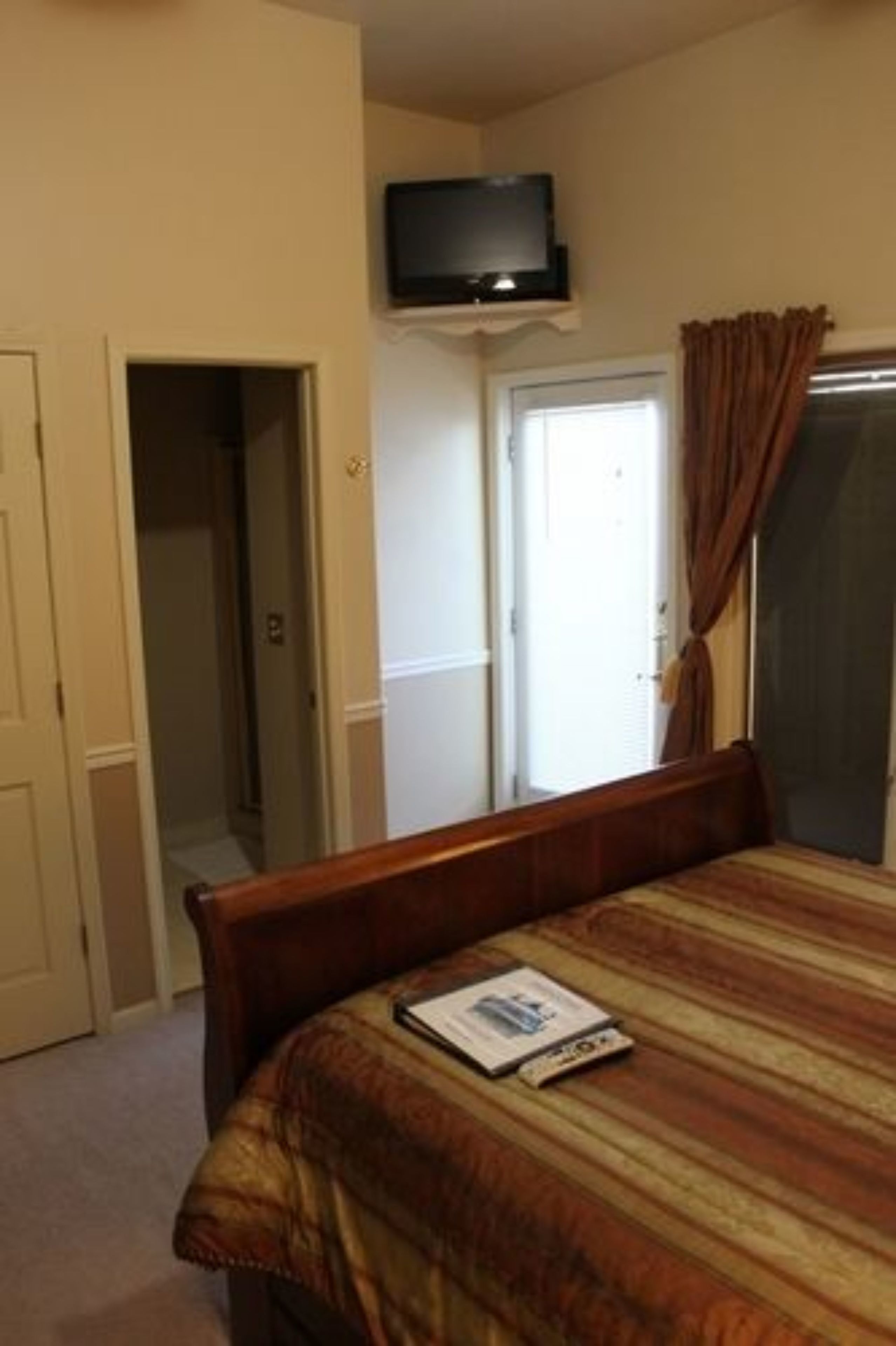 Quarto de hotel com uma cama, televisão na parede, porta para um banheiro e uma janela com cortinas.