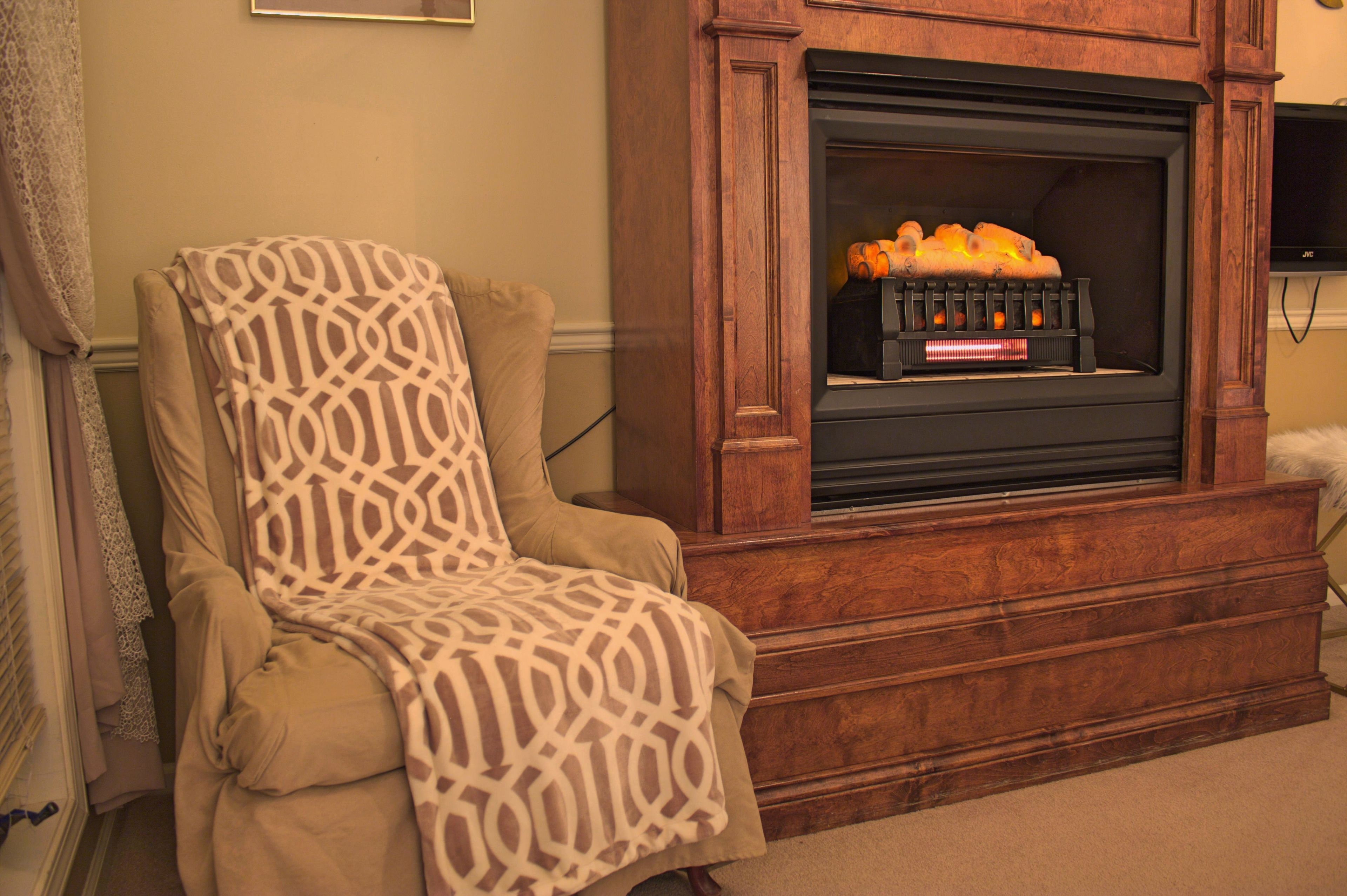 A living room with a fireplace, a patterned armchair, and a television mounted on the wall.