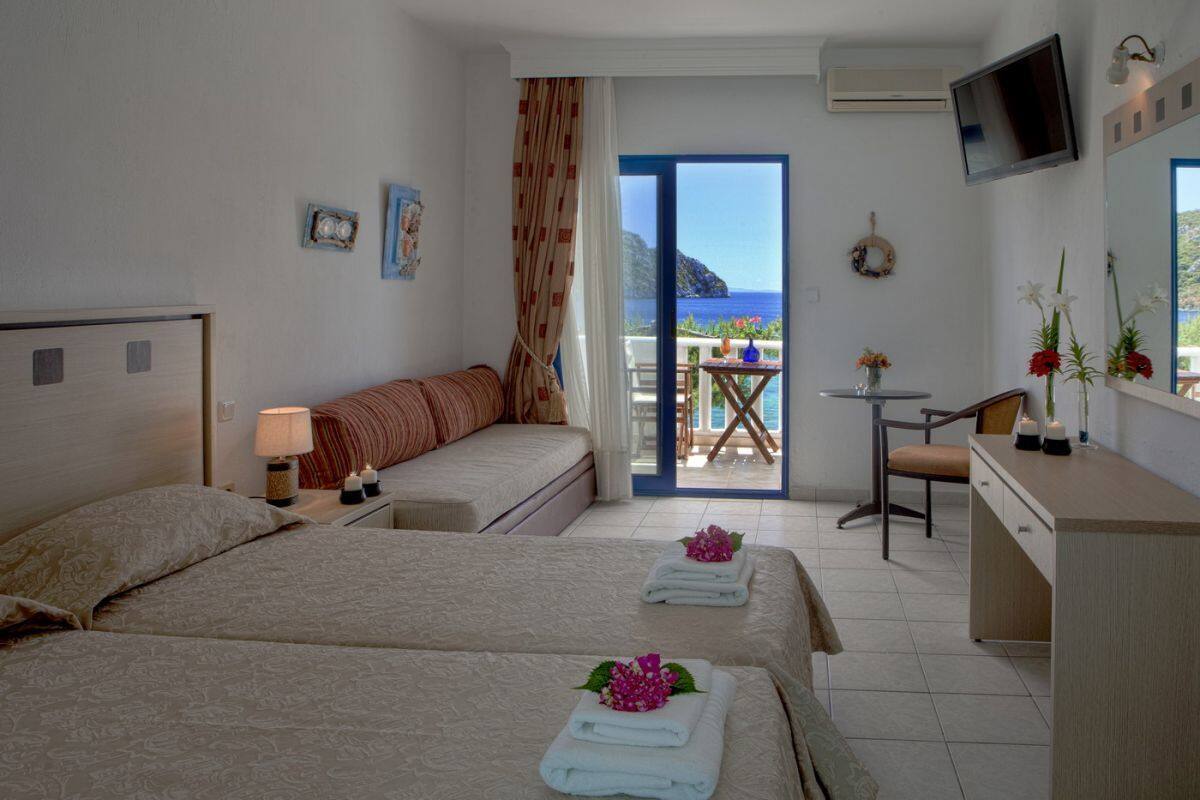 Une chambre d’hôtel avec deux lits, un bureau, une chaise, une télévision et un balcon donnant sur la mer.