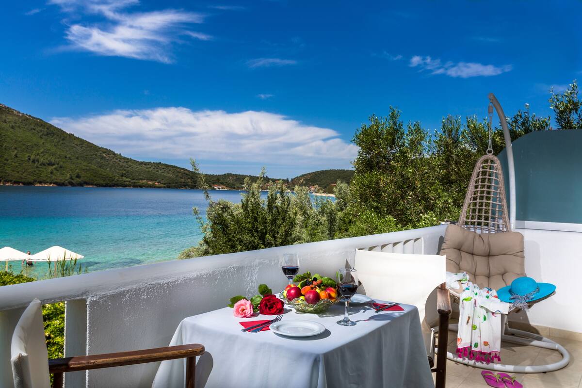 Un balcon avec une table dressée pour deux personnes, donnant sur une étendue d’eau et une végétation luxuriante.