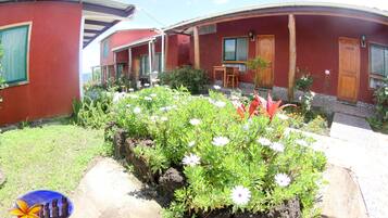 A red building with a covered patio area, a small garden with white flowers, and a logo in the bottom left corner.
