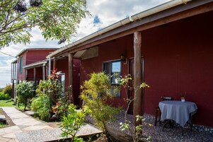 Un edificio rojo con un porche cubierto, un patio con baldosas y una mesa con una silla.