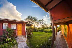 Una casa rústica con puerta de madera, un jardín con terraza de madera y cielo despejado.