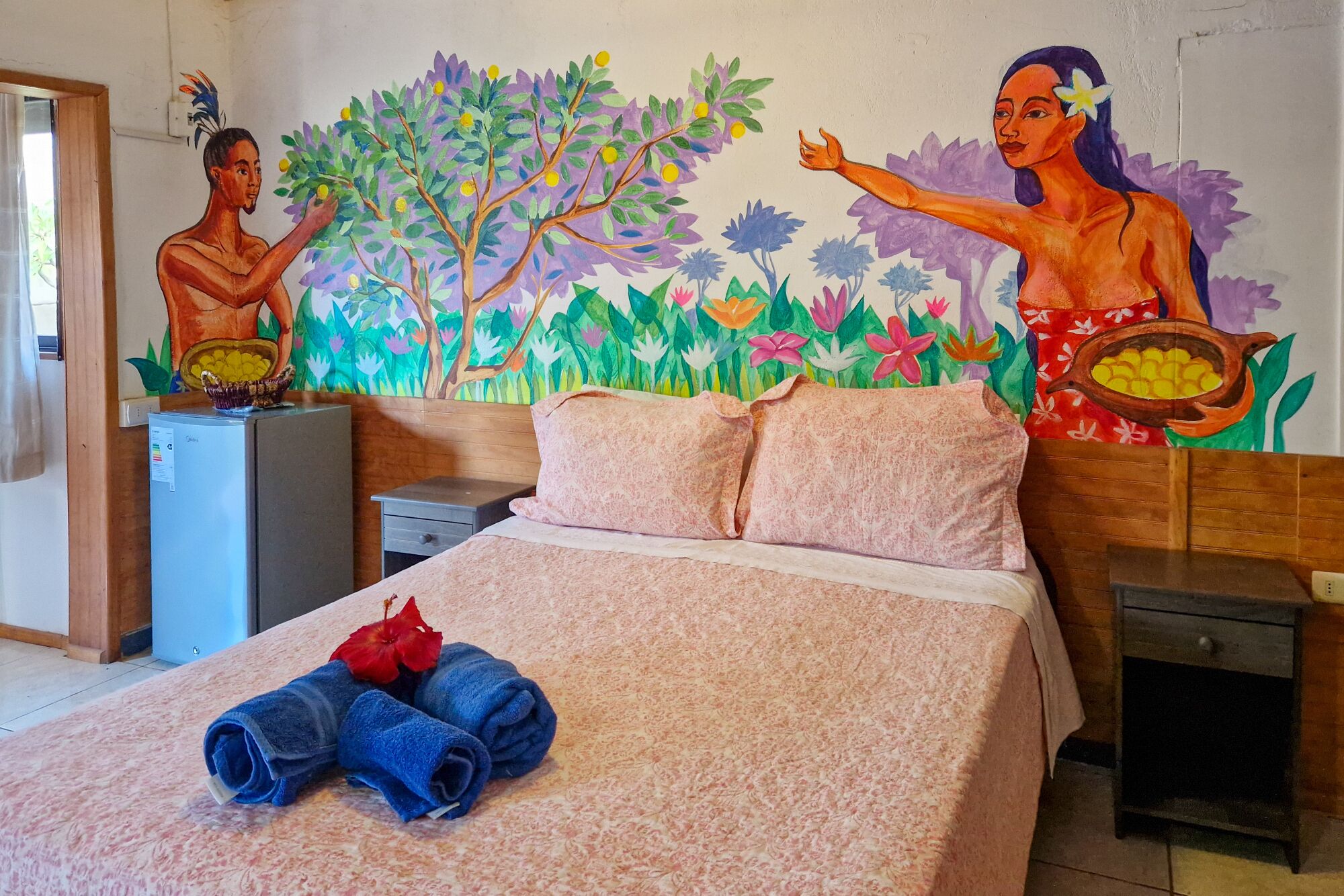 A hotel room with a bed, a nightstand, a desk, and a wall mural.