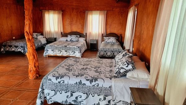 Una habitación tipo cabaña de madera con cuatro camas, cada una con ropa de cama estampada, y un robusto pilar de madera.