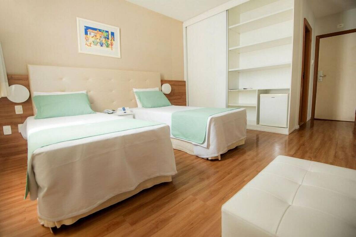 Een hotelkamer met twee bedden, een houten vloer, een witte inbouwkast en een klein kastje.