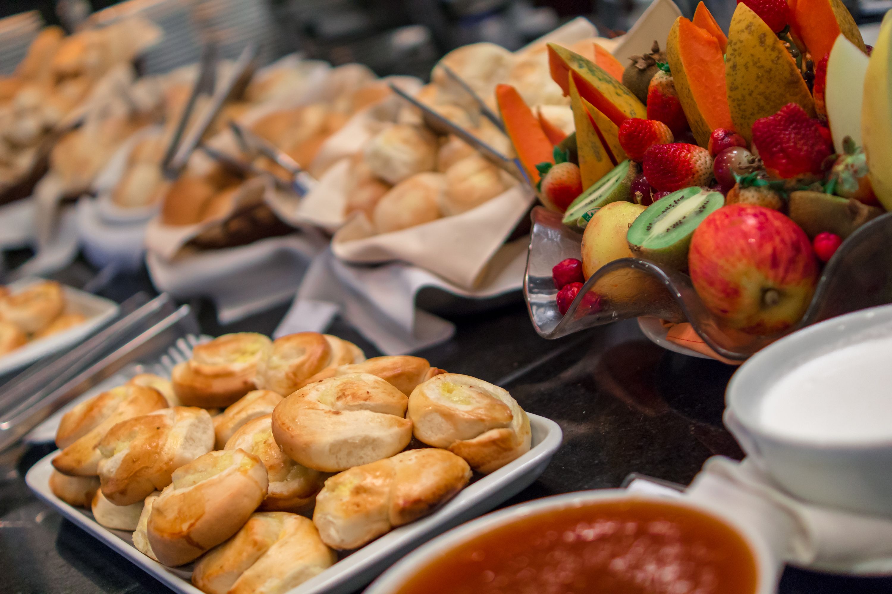 A buffet with various food items including pastries, fruits, and a bowl of sauce.