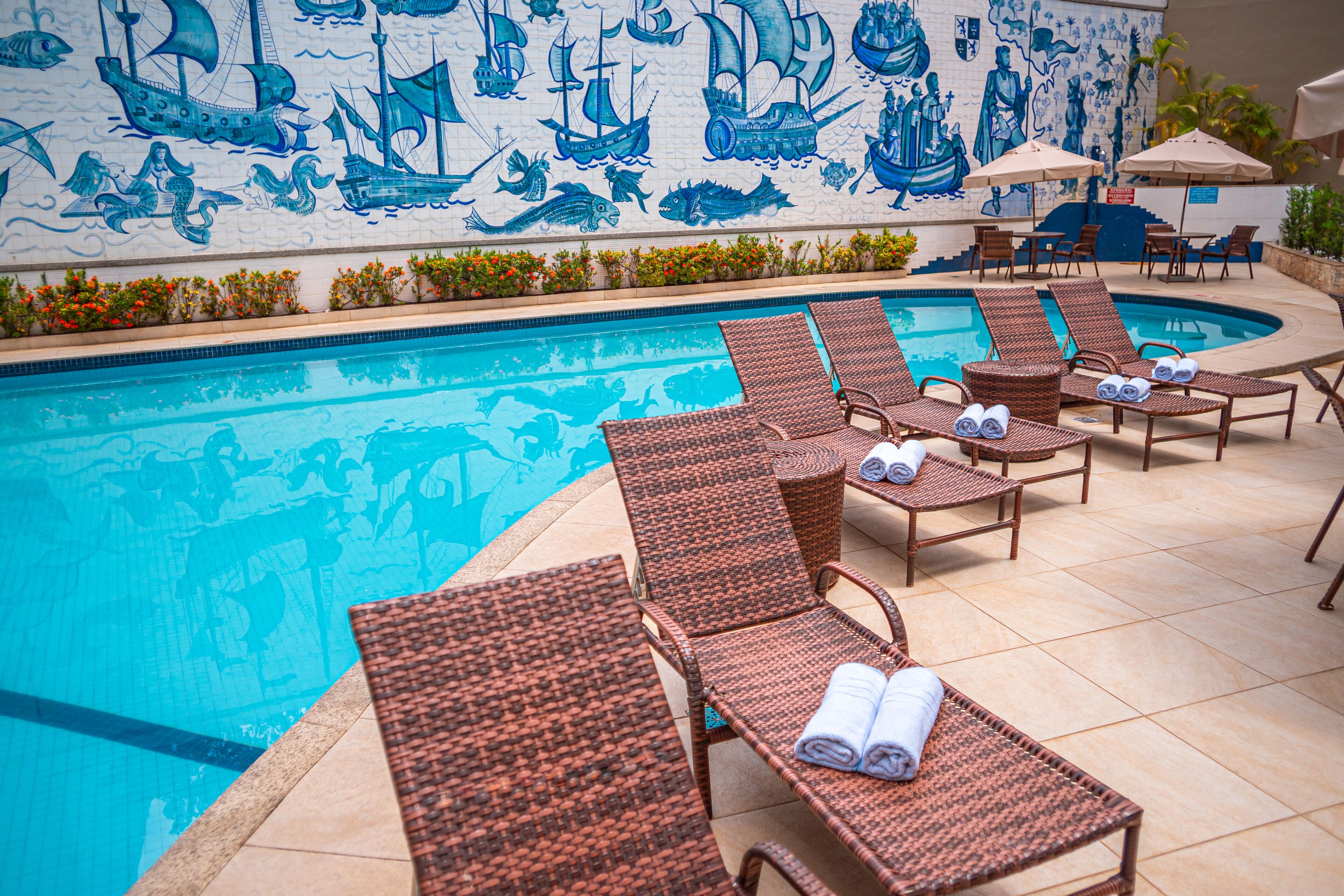 A pool area with lounge chairs and a mural of ships and mermaids.