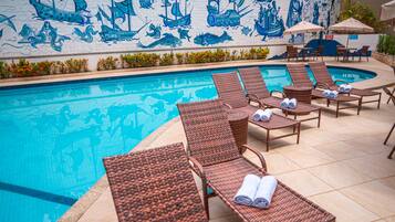 Área de piscina com espreguiçadeiras e um mural de navios e sereias.