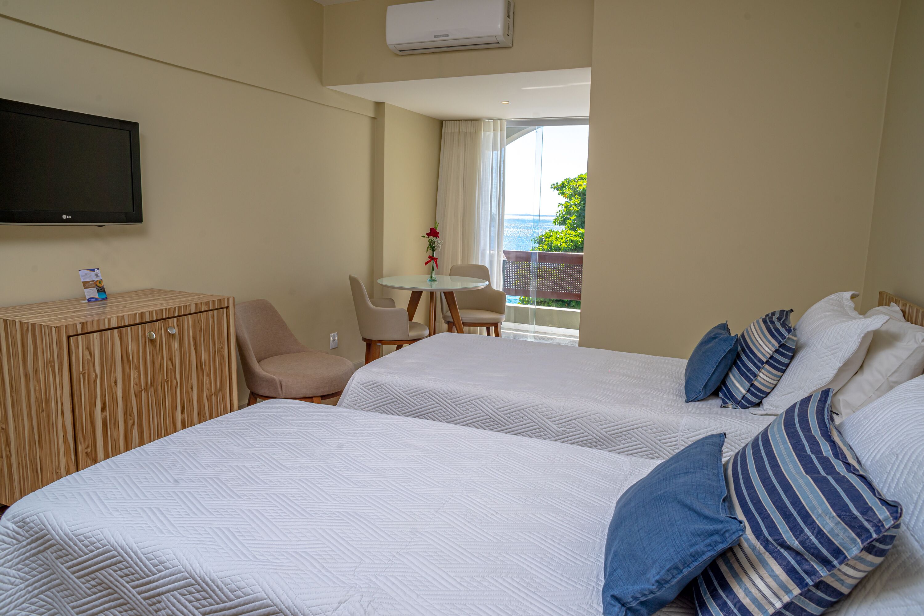 A hotel room with two beds, a TV, a small table with chairs, and a view of the outdoors.