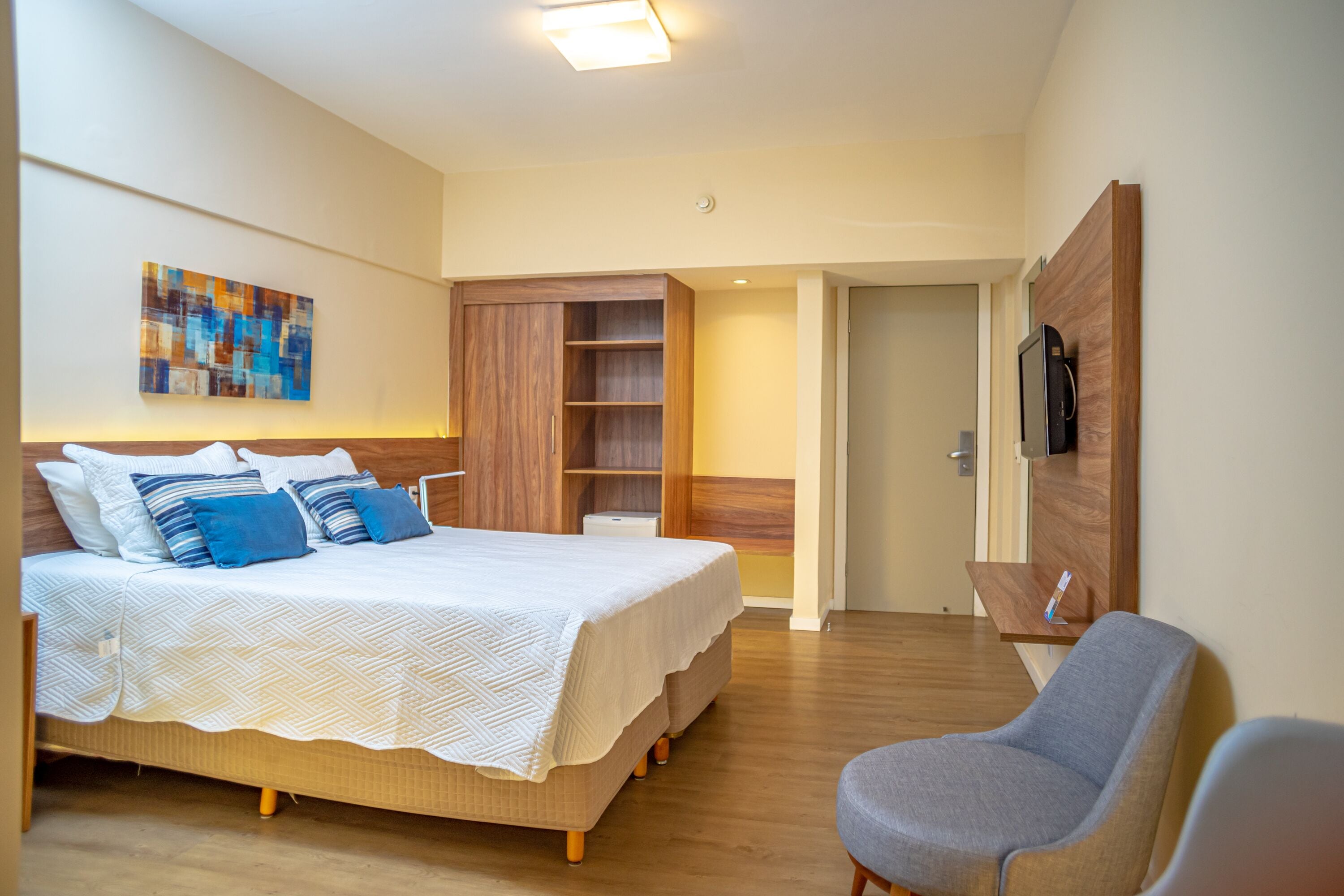 A modern hotel room with a large bed, a wardrobe, a TV, and a seating area.