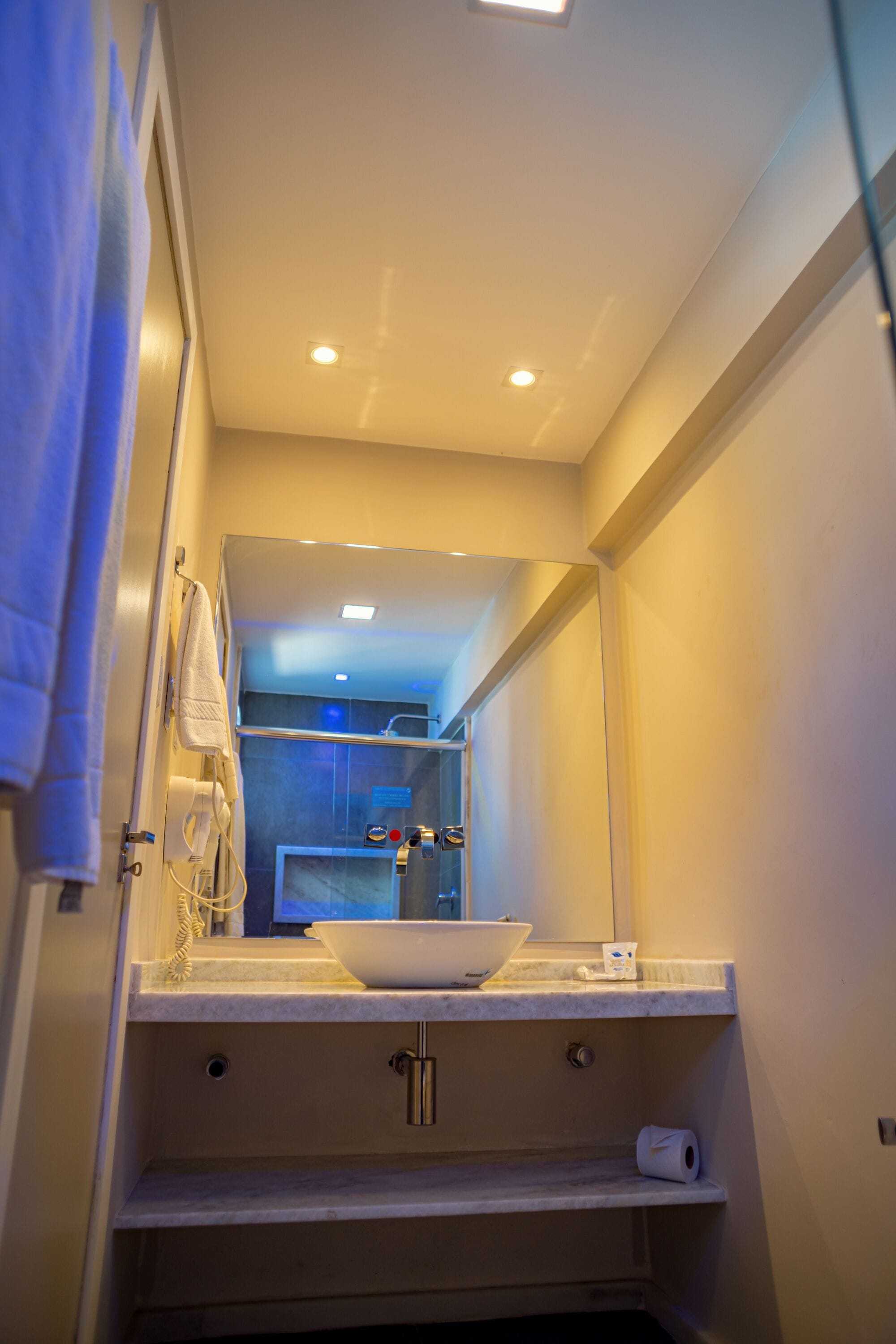 A bathroom with a sink, mirror, towel rack, and a toilet paper holder.