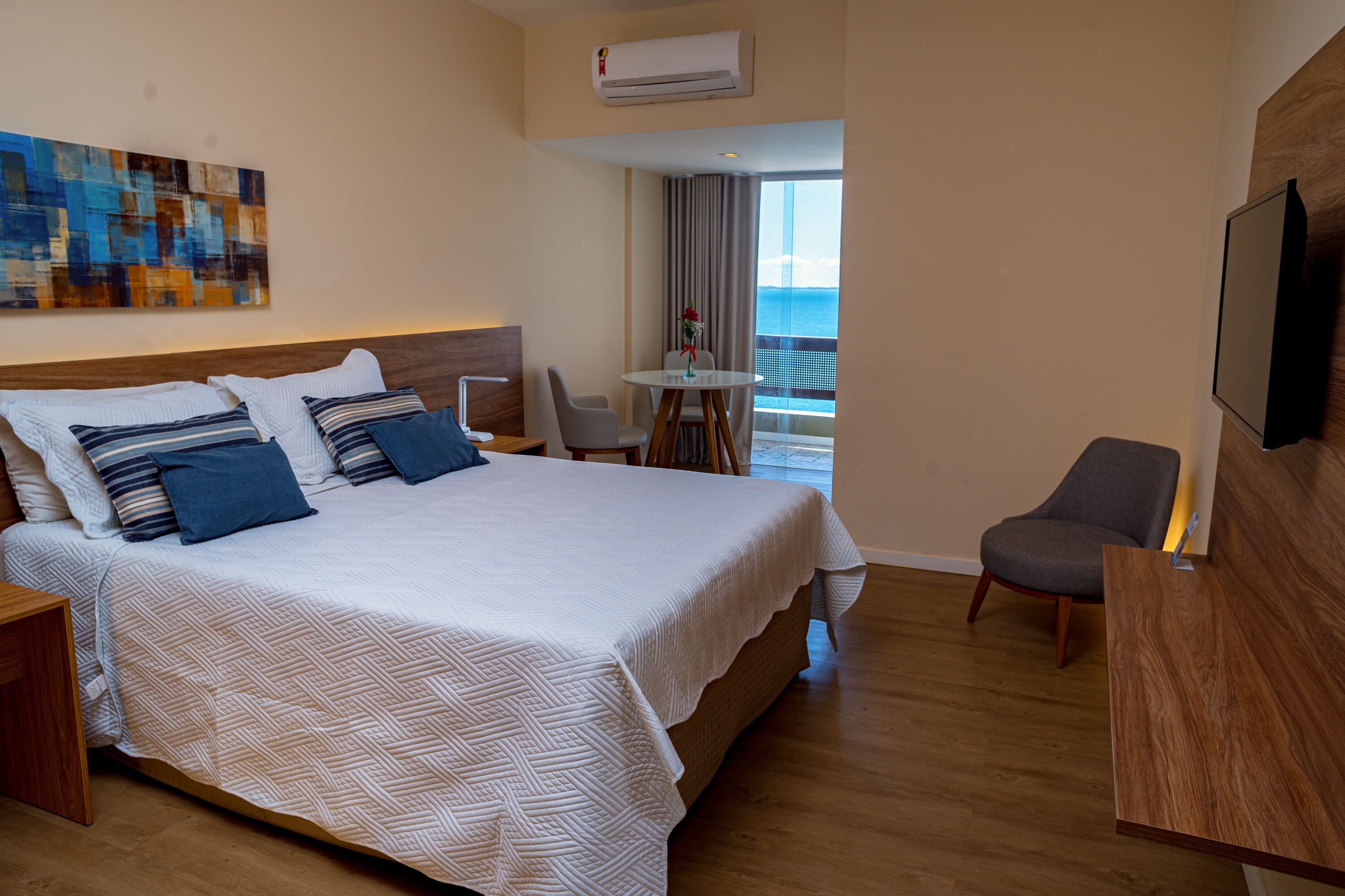 A hotel room with a large bed, a desk, a chair, a TV, and a balcony with a view.