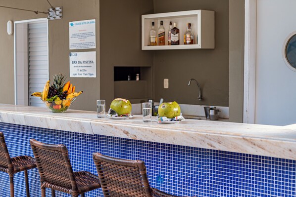 A bar area with a tiled pool, wicker chairs, a fruit bowl, and a shelf with bottles. - Grande Hotel da Barra (Salvador)