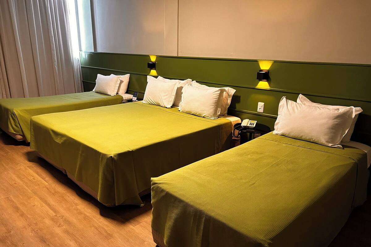 Een hotelkamer met twee eenpersoonsbedden, elk met een groene sprei en witte kussens. Aan de rechterkant van de bedden staat een bedtafel met een telefoon.