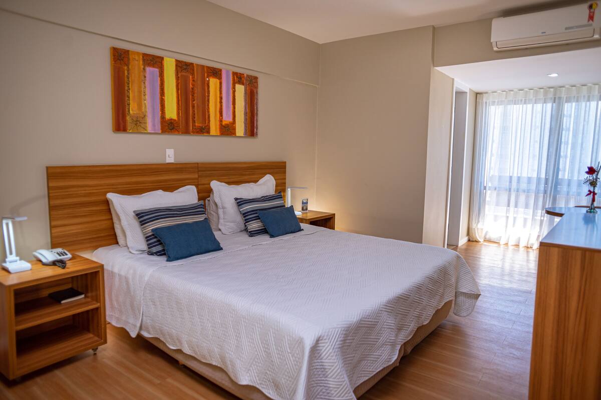 Een keurig opgemaakte hotelkamer met een groot bed, nachtkastjes, een bedlampje en uitzicht op het landschap door een raam.
