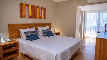 Una cama bien hecha con una colcha blanca y almohadas azules, un cabecero de madera, una mesita de noche con una lámpara y una obra de arte colgada en la pared.
