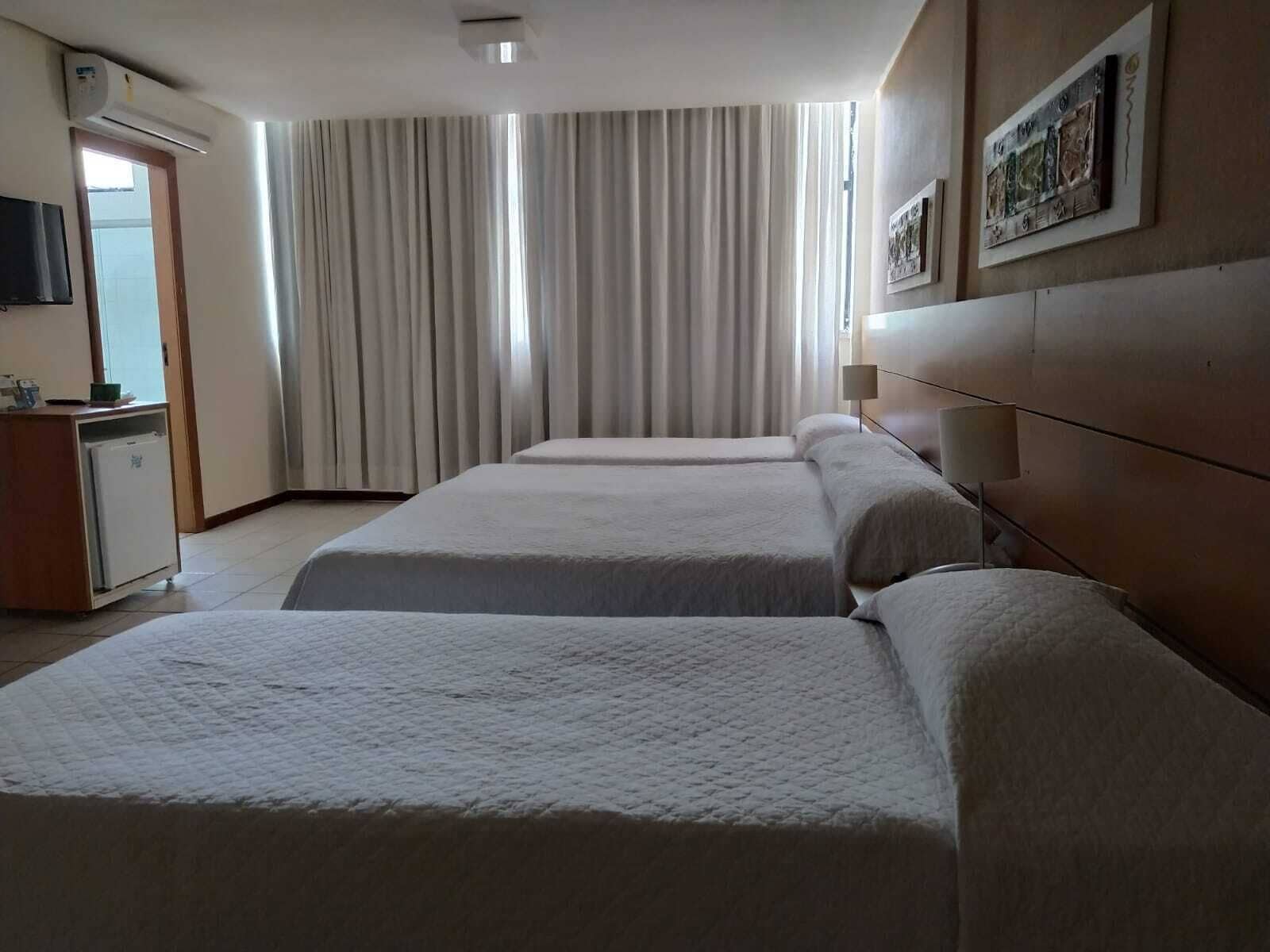 A hotel room with two beds, a desk with a refrigerator, a TV, and a large window with curtains.
