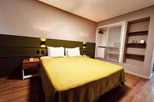 Una habitación de hotel con cama, mesitas de noche, armario y mesilla.