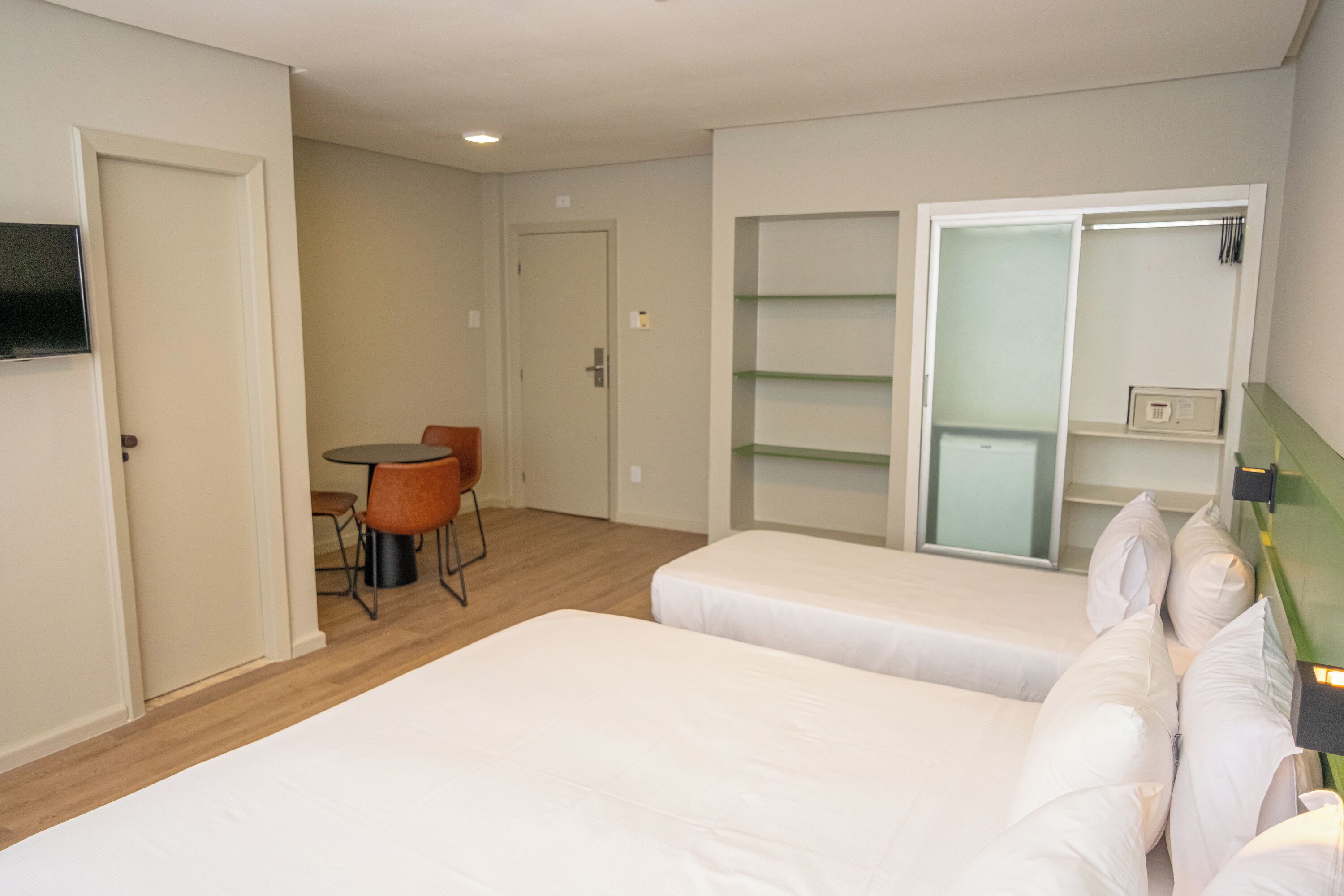 A hotel room with two beds, a dining table with chairs, a small kitchen area, and a sliding glass door closet.