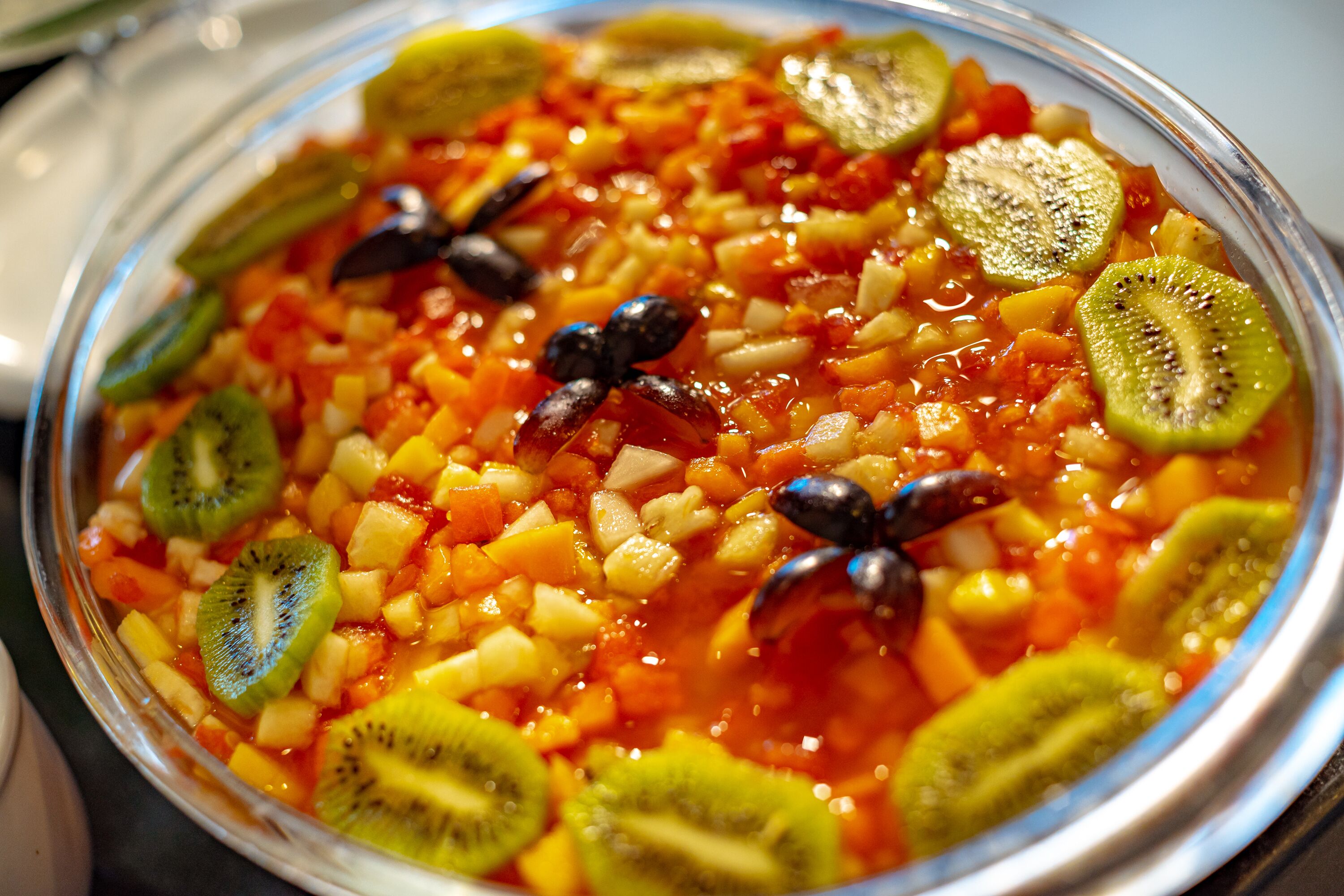 A bowl of fruit salad with kiwi slices and olives.