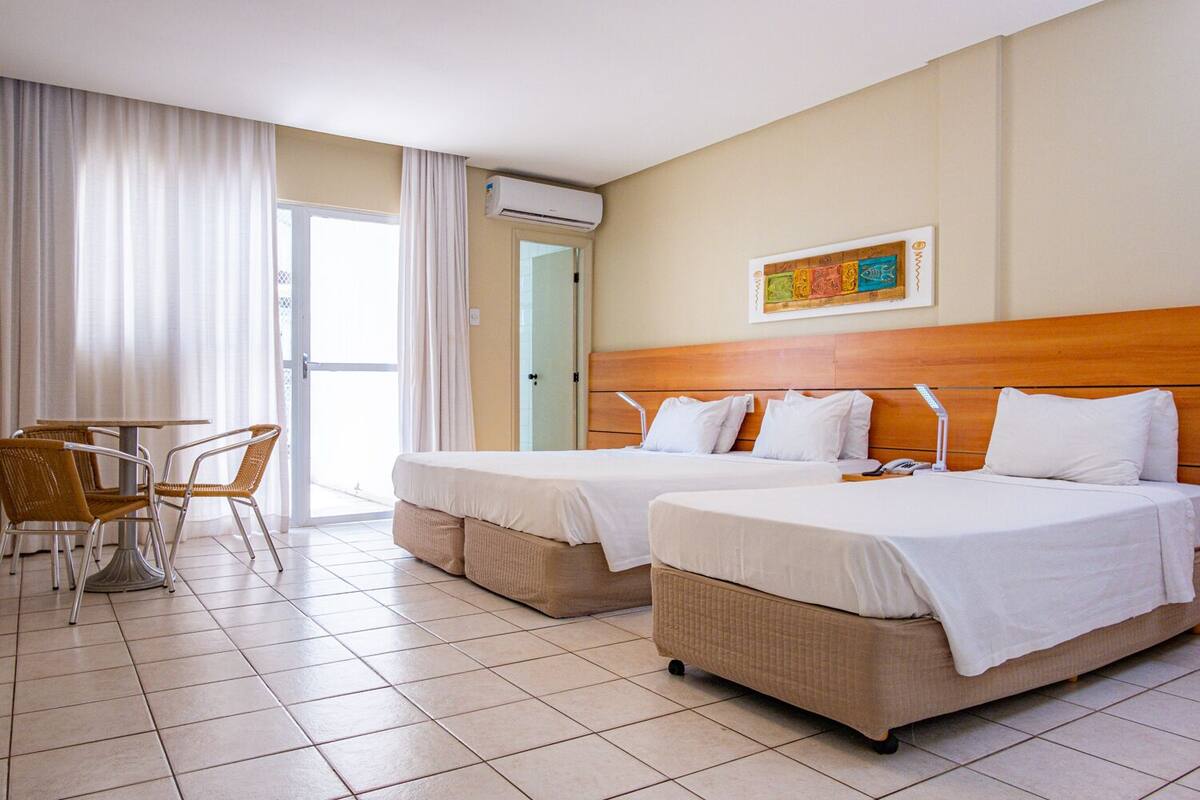 Een hotelkamer met twee bedden, een eettafel met stoelen en een airconditioner.