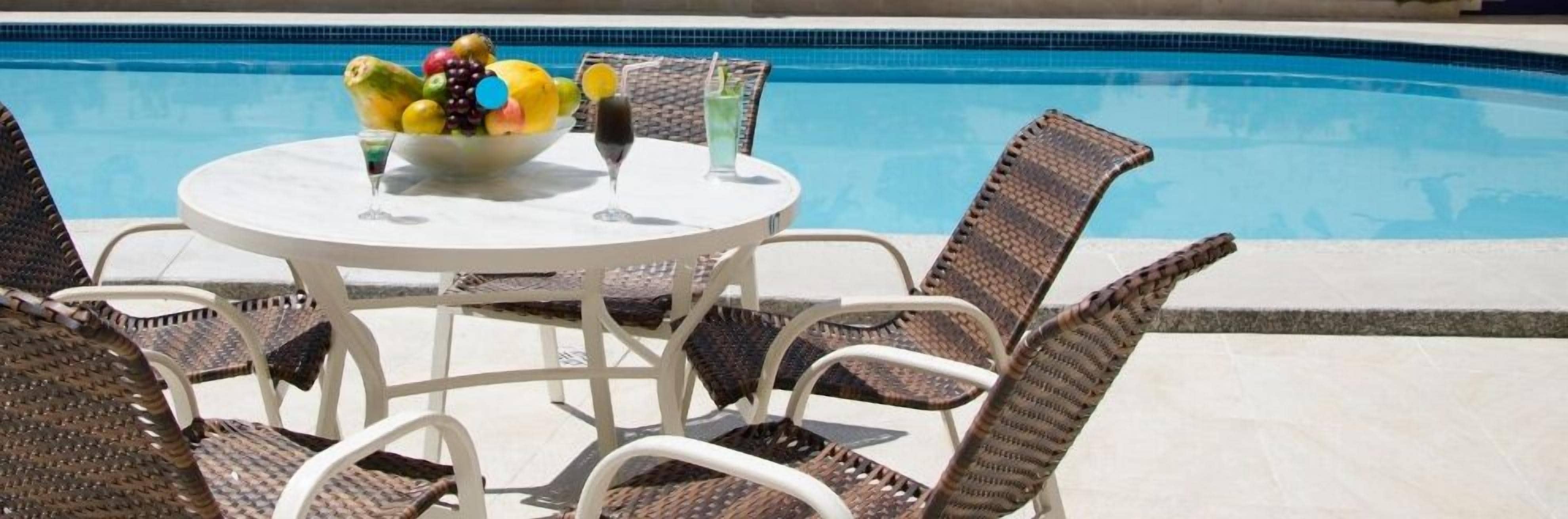 Mesa junto a la piscina con sillas de mimbre y un frutero.