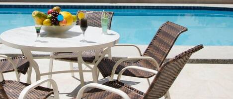 Mesa junto a la piscina con sillas de mimbre y un frutero.