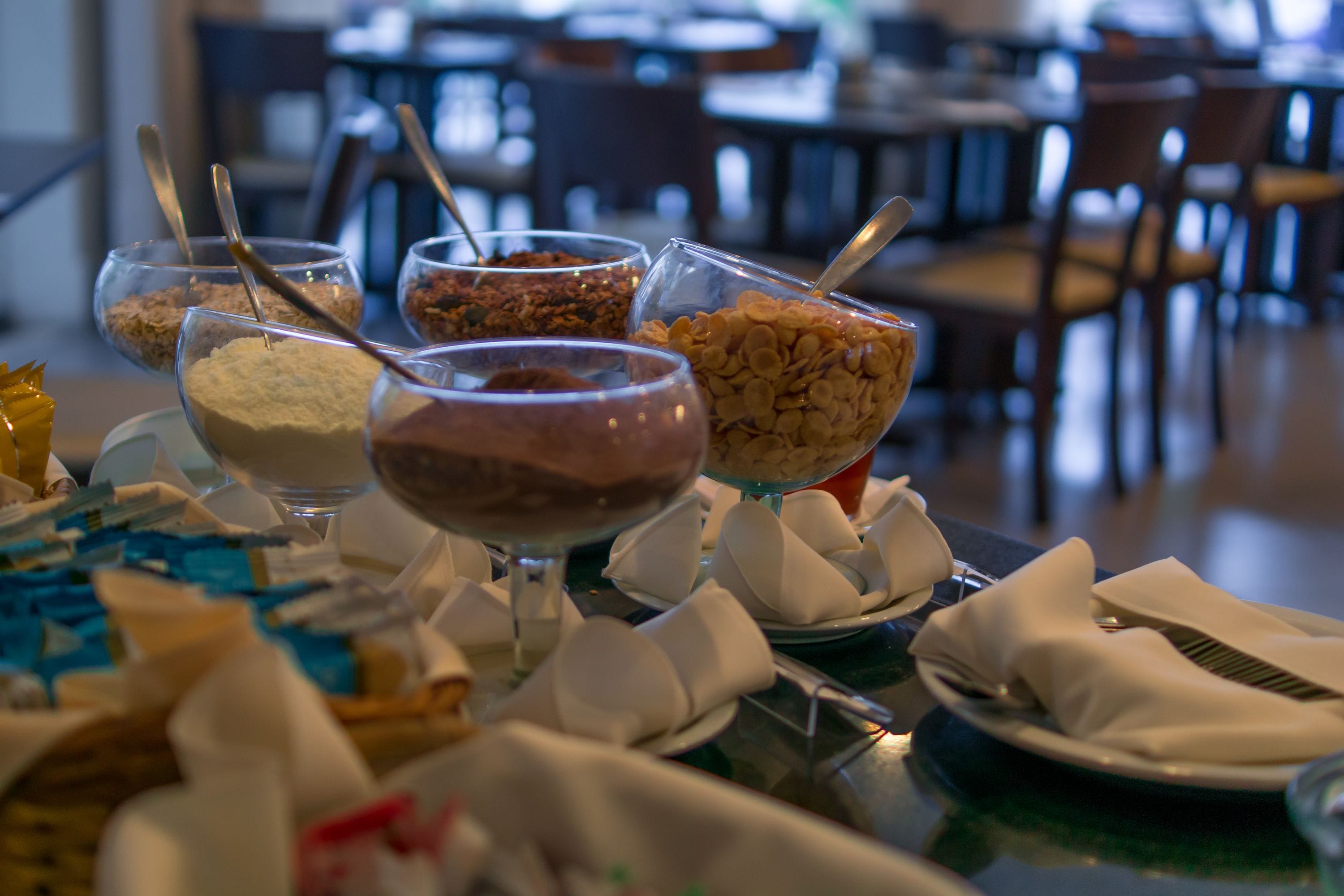 Una mesa de buffet con diversos alimentos en cuencos y vasos, con cubiertos dentro.