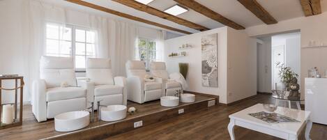 Un salón espacioso con techo de madera, sofás blancos, una mesa de centro y un amplio ventanal con cortinas.