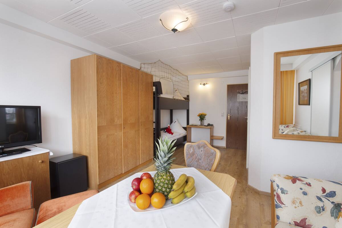 A compact room with a bunk bed, a television, a small table with fruit, and a floral armchair.