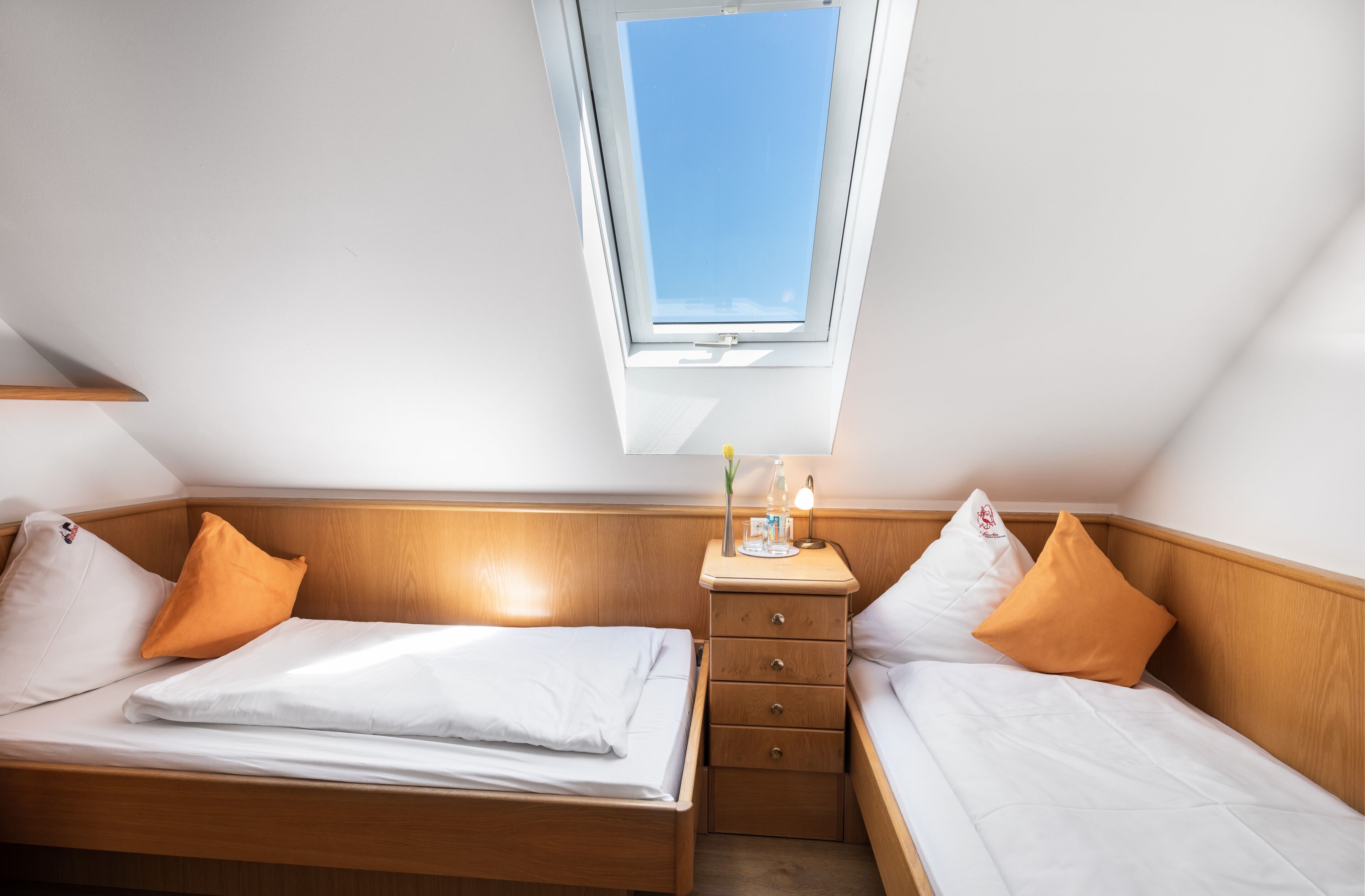 A small, well-lit room with two beds, a nightstand, and a skylight.