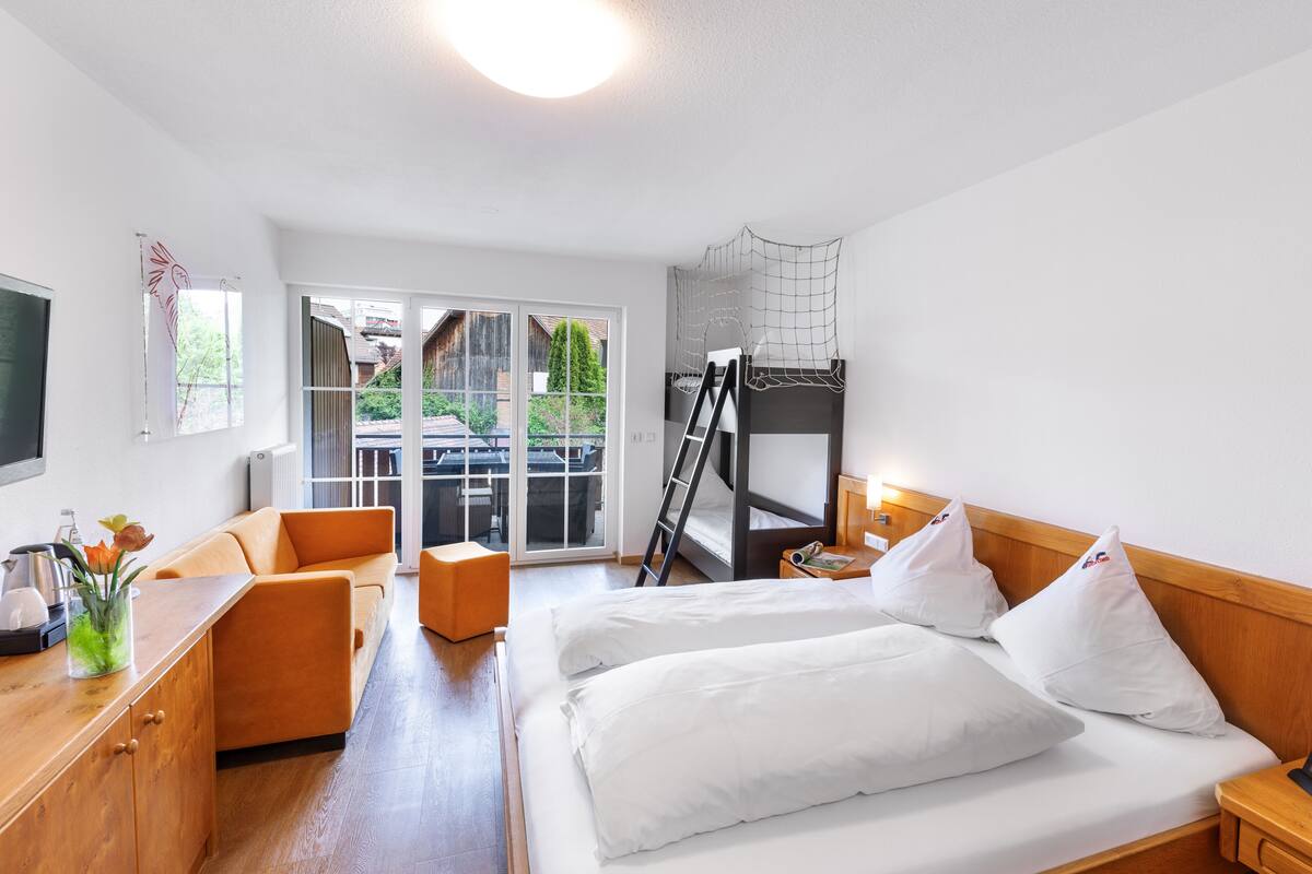 A hotel room with a bunk bed, a desk with a chair, a small table with a lamp, and a TV.