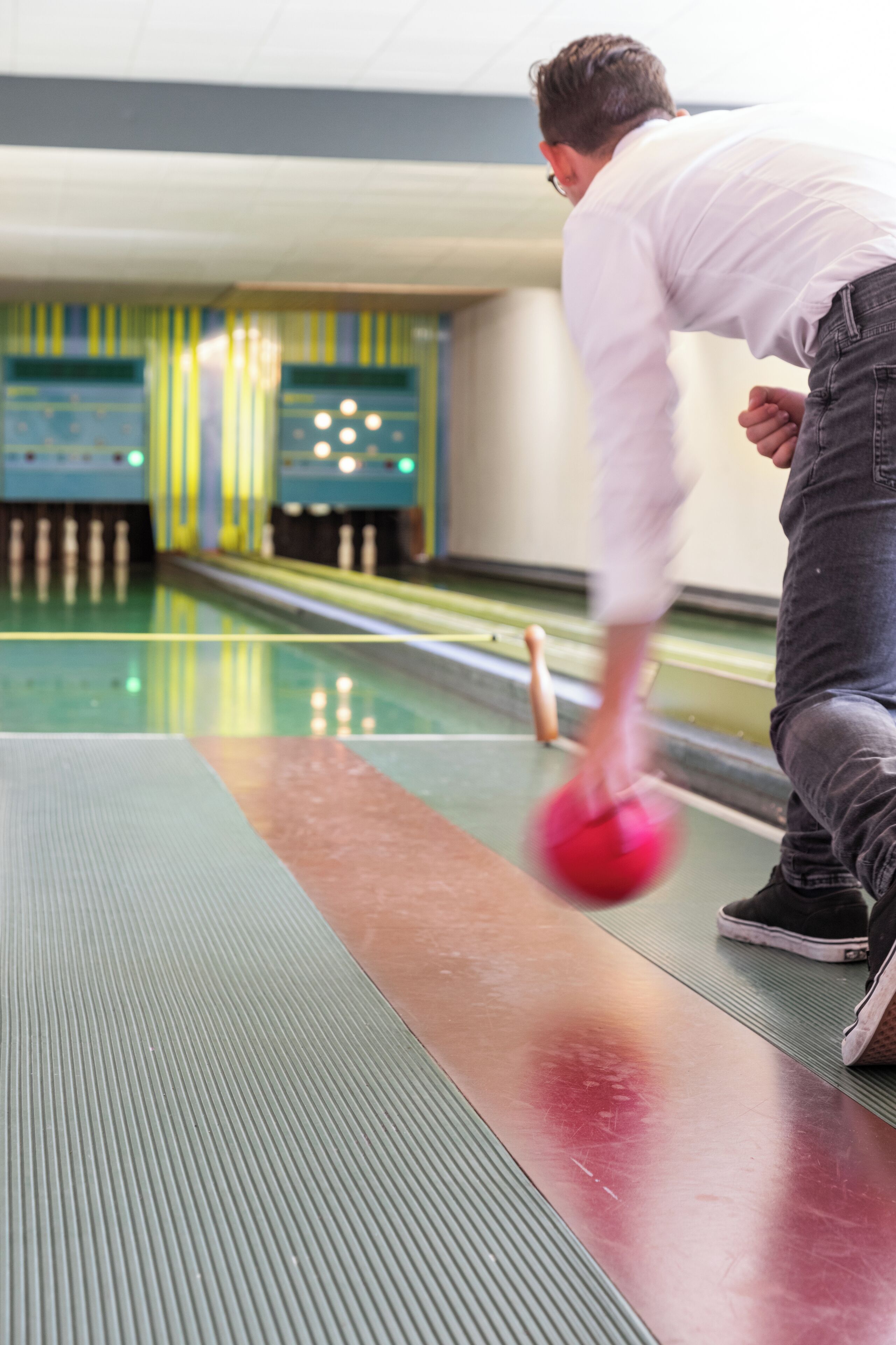 Eine Kegelbahn mit Bahnen, einem Bowlingball und einer Person in weißem Hemd und Jeans.
