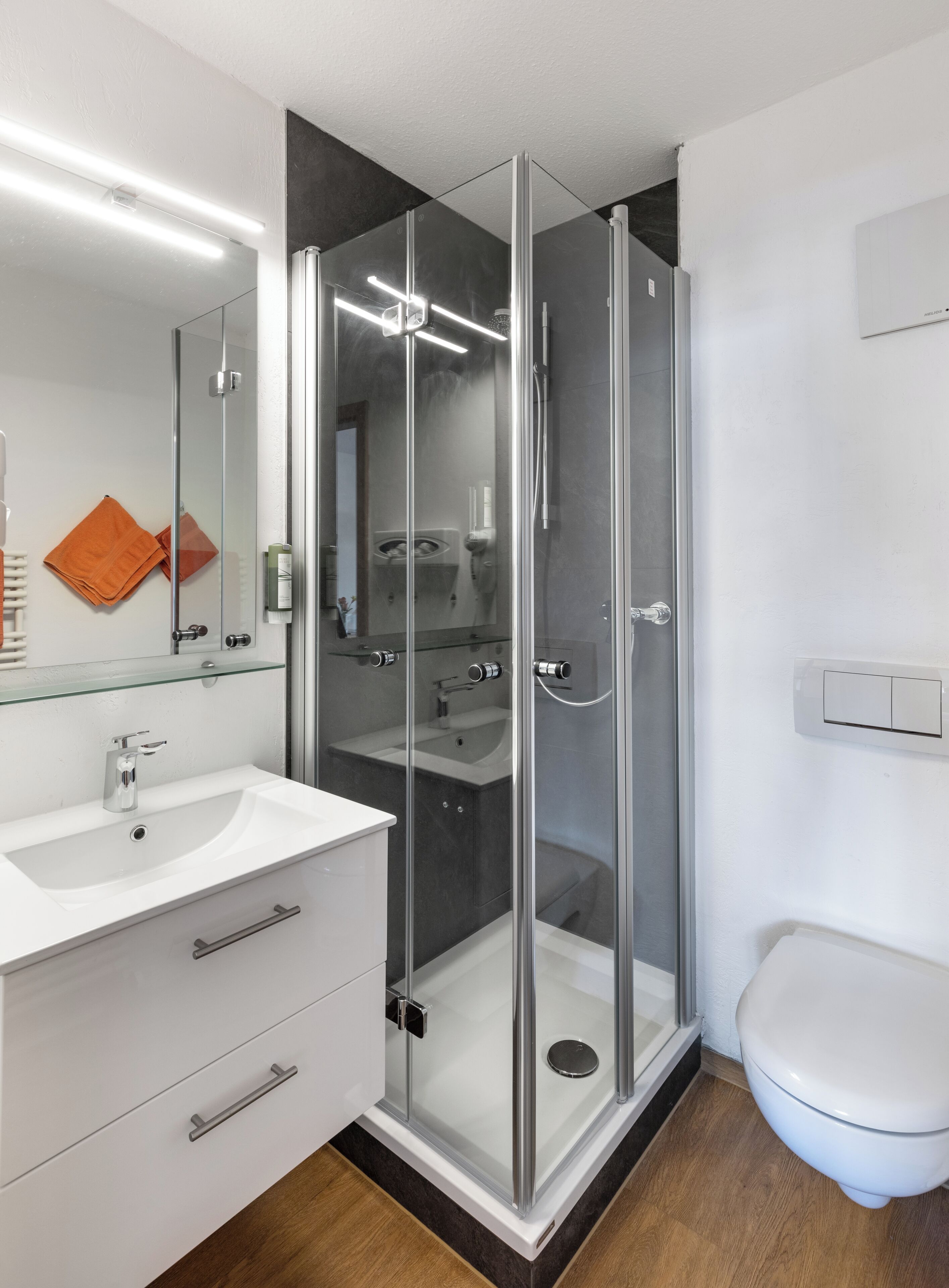 Uma casa de banho moderna com chuveiro envolto em vidro, lavatório branco e sanita.