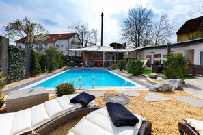 A swimming pool with lounge chairs and a covered area, surrounded by a landscaped garden and residential buildings. - Bodensee Hotel Storchen (Uhldingen-Muehlhofen)
