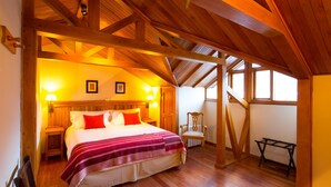 A bedroom with a wooden ceiling, a bed with a striped blanket, two bedside lamps, and a chair. - Hostería Senderos (El Chalten)