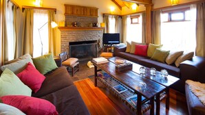 A cozy living room with a fireplace, wooden beams, and comfortable seating. - Hostería Senderos (El Chalten)