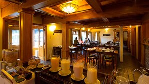 A restaurant with wooden interiors, multiple dining tables, and a buffet area with various food items. - Hostería Senderos (El Chalten)