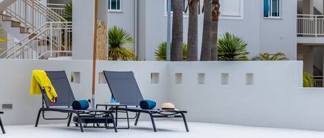 A swimming pool area with lounge chairs, a sun umbrella, and a staircase leading to an upper level.