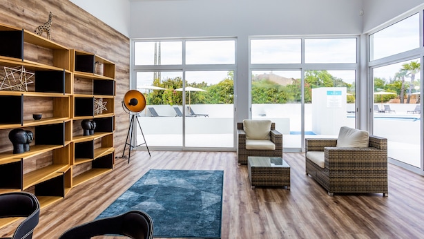 Un interior moderno con pared de madera, un ventanal grande, muebles de mimbre y un tapete azul.