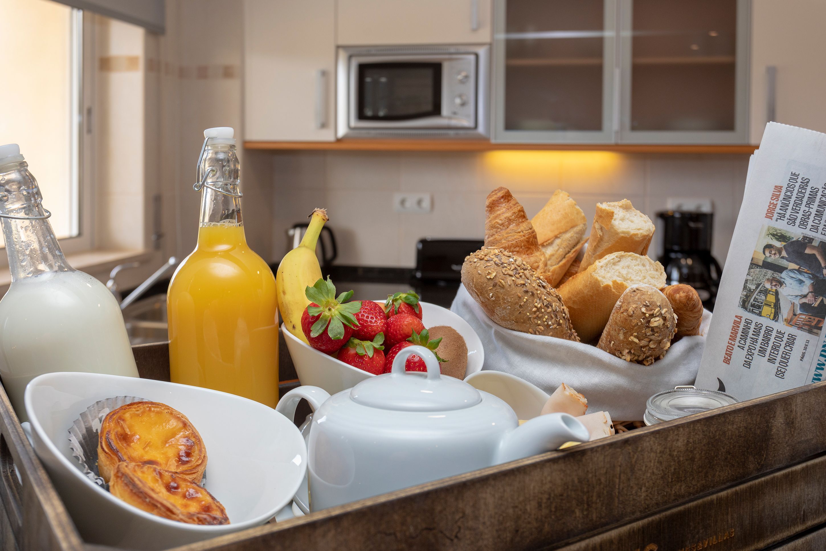 A breakfast tray with bread, strawberries, a bottle of orange juice, and a teapot.