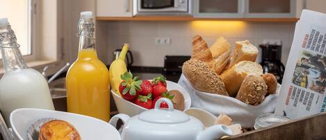 A breakfast tray with bread, strawberries, a bottle of orange juice, and a teapot.