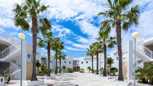 Un patio con palmeras, un edificio blanco con balcones y un cielo azul despejado.