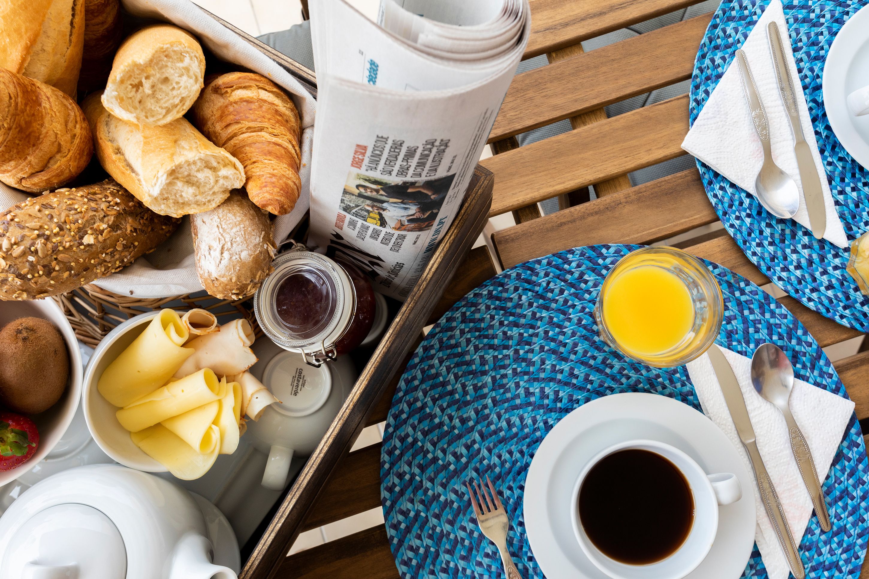 Un vassoio da colazione con croissant, pane, marmellata, formaggio e un giornale.