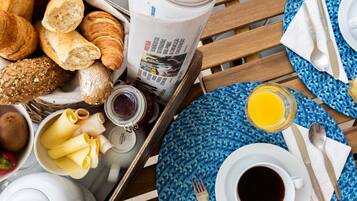 A breakfast tray with croissants, bread, jam, cheese, and a newspaper.