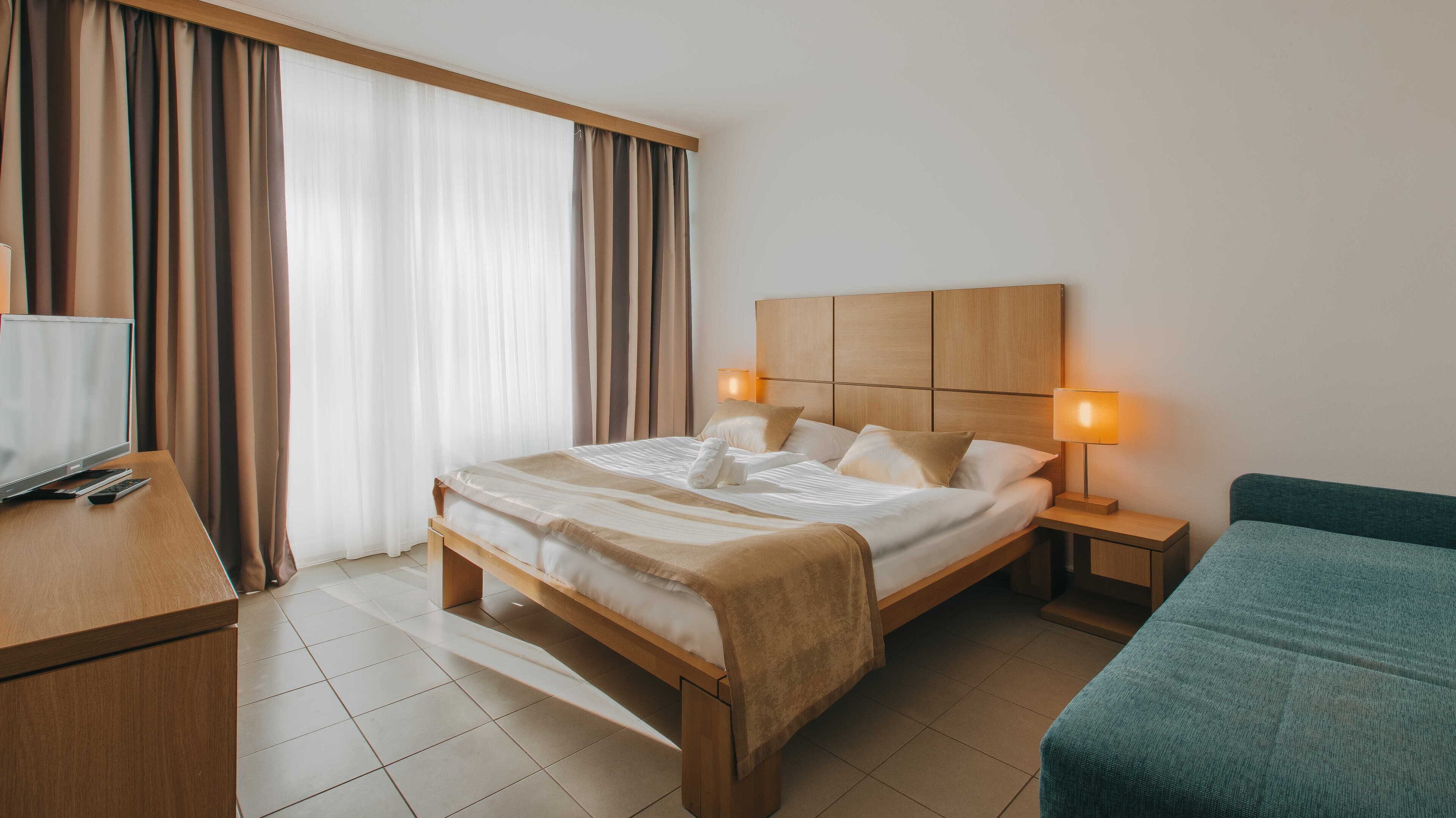 Hotellihuone, jossa on sänky, yöpöydät, työpöytä ja televisio.