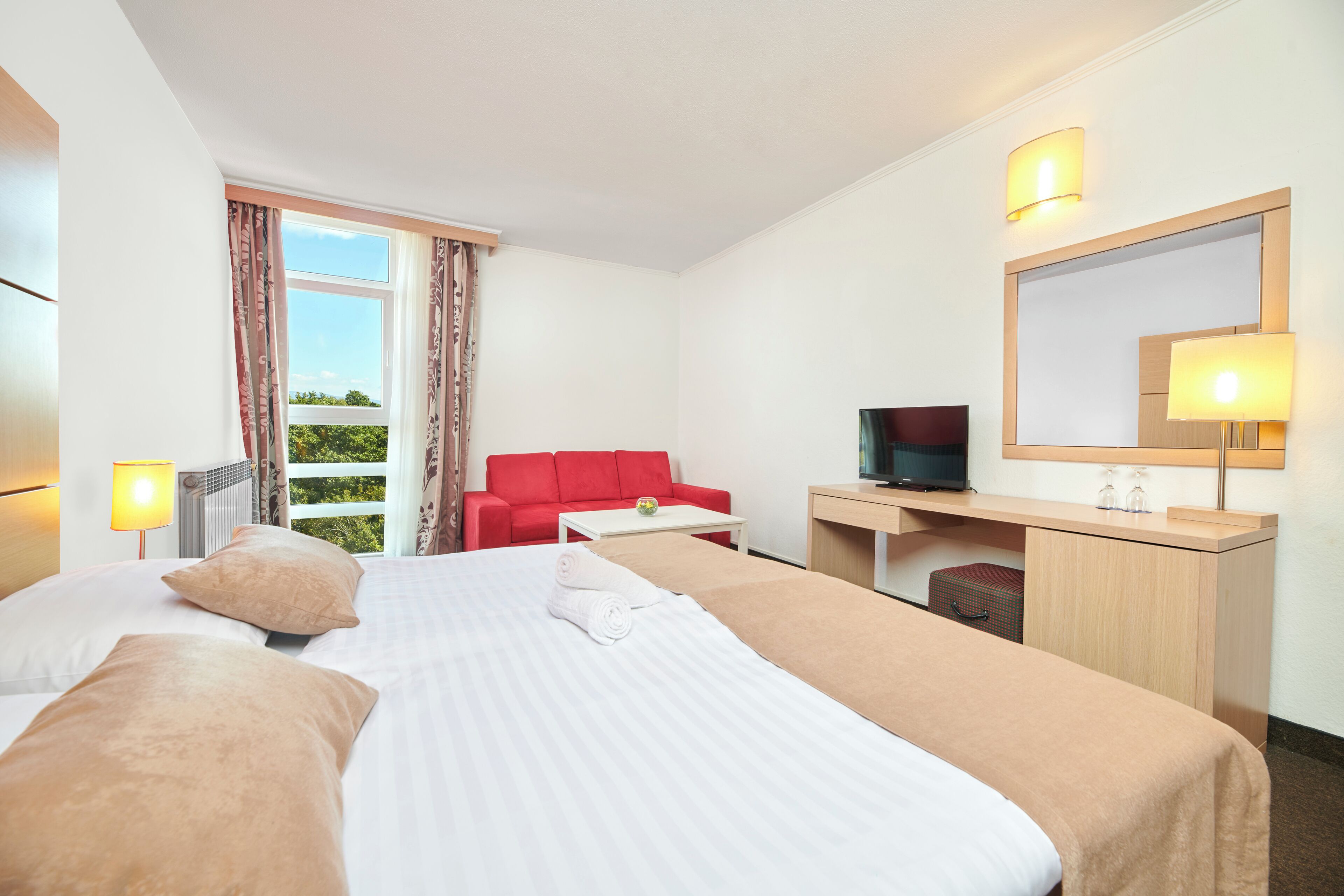 Una habitación de hotel con una cama, un escritorio, un televisor y un sofá rojo.