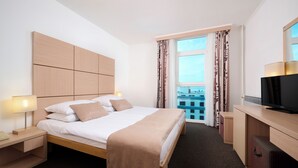 A hotel room with a bed, bedside tables, a TV, and a view of the city through the window. - Magal Maradiso Hotel by Aminess  (Omisalj)